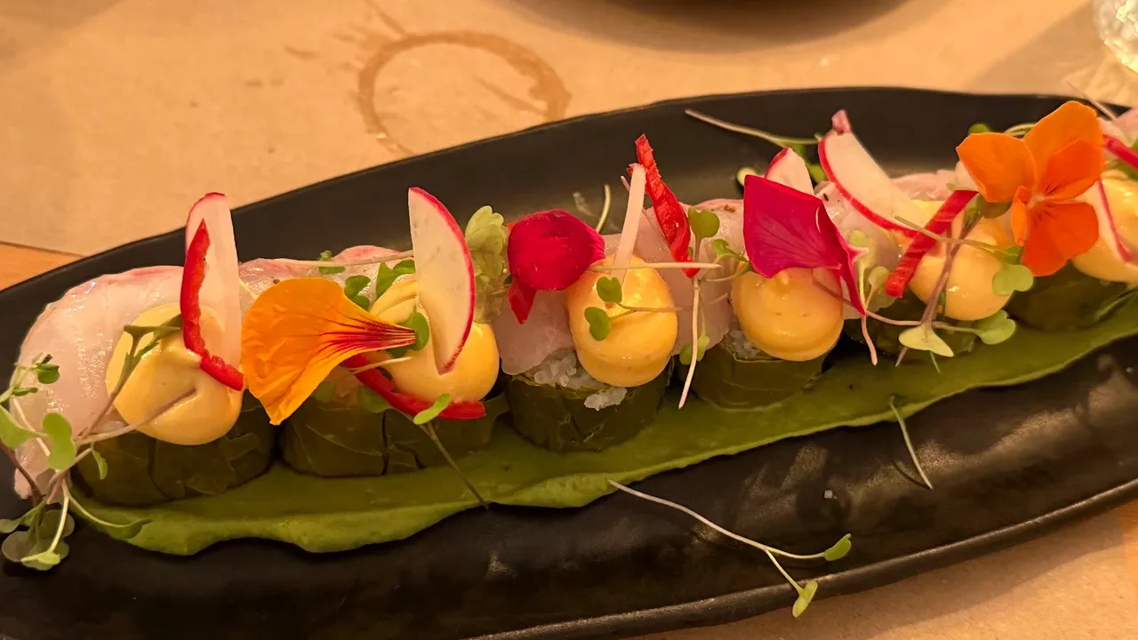 An elegant plated dish of vine-leaf parcels with seabass and edible flowers on a dark plate at a Thessaloniki fine-dining restaurant