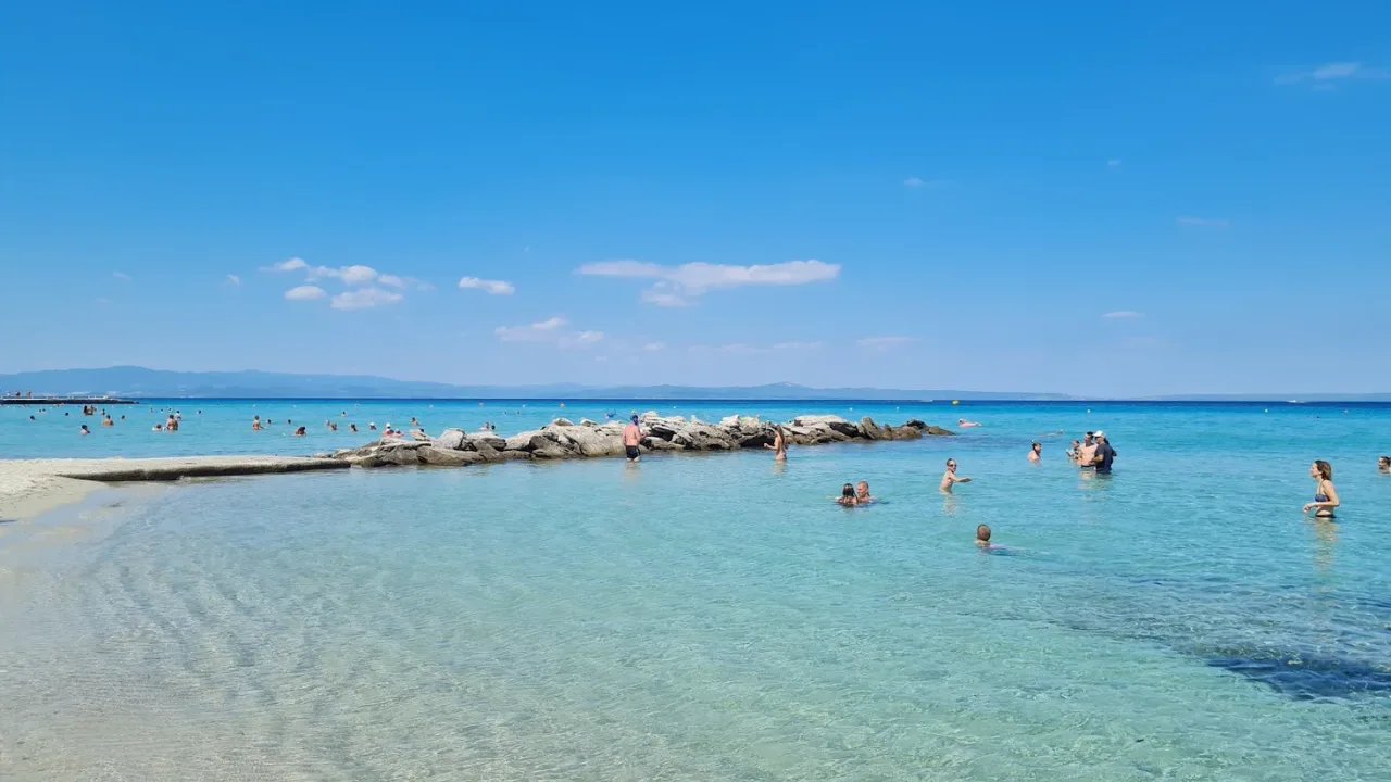 A turquoise beach with clear shallow water and swimmers near Thessaloniki on a bright summer day