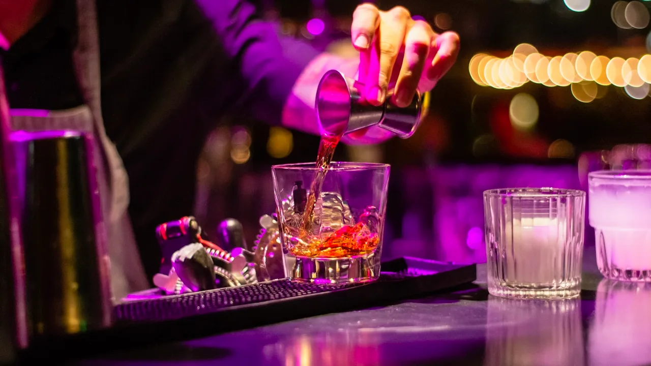 A bartender mixing a cocktail under neon light in a dimly lit bar