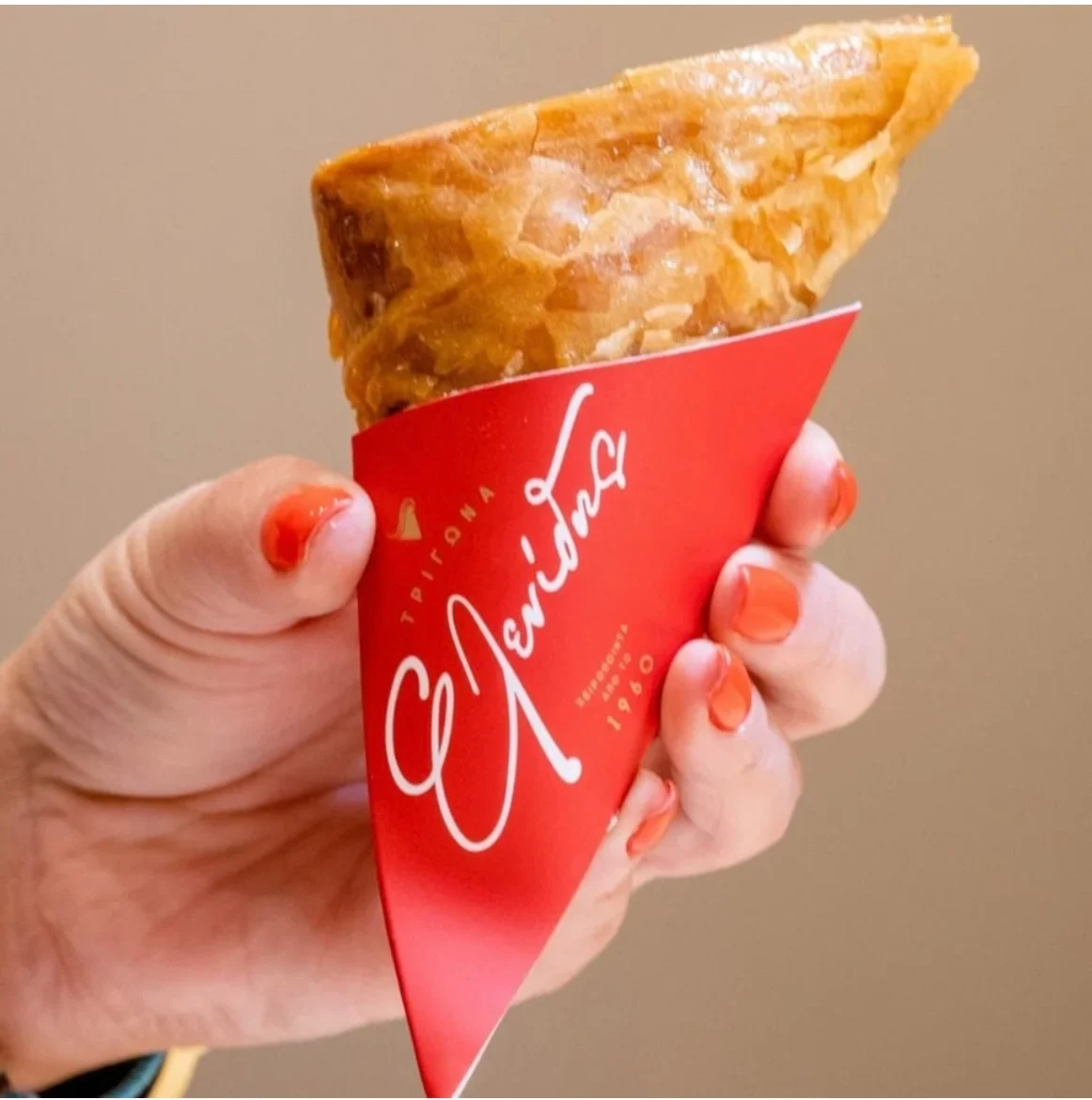 A custard-filled trigono panoramatos in its red Trigona Elenidis paper cone, held in hand, Thessaloniki