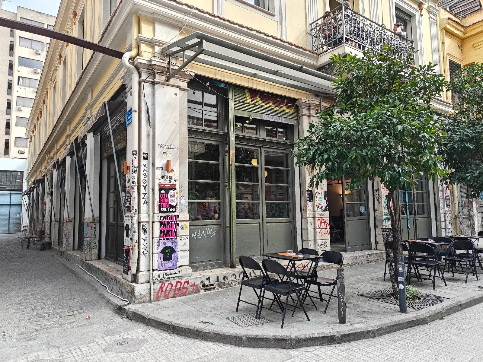 The bohemian corner building of Ypsilon café-bar in central Thessaloniki — columns layered with posters and street art, café tables out front