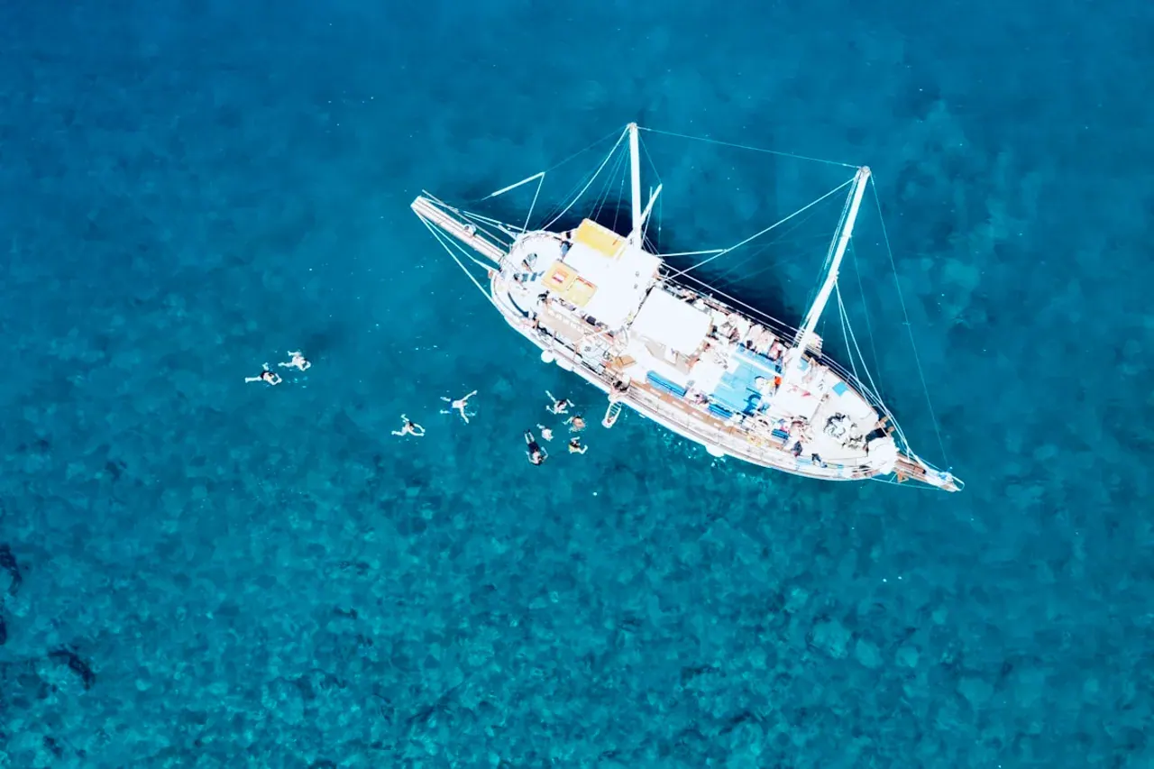 A traditional wooden cruise boat anchored on the clear blue gulf, swimmers in the water around it
