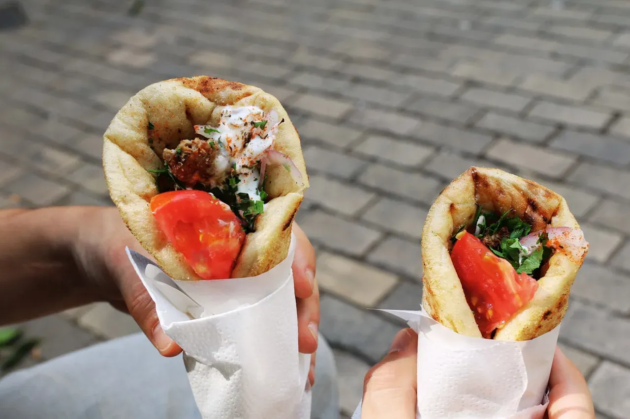 Two freshly wrapped gyros pitas held over a cobbled street