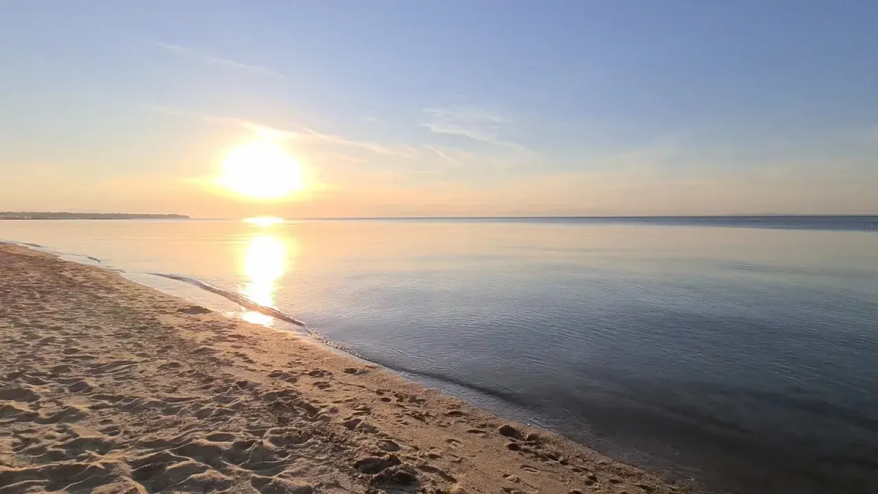 The wide sandy beach and calm, shallow water of the Thermaic Gulf at golden hour near Thessaloniki