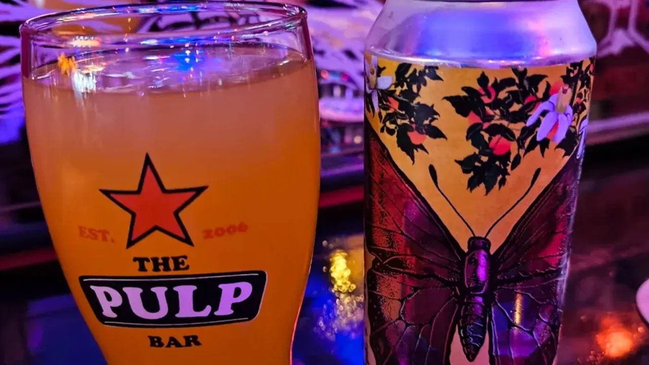 A branded Pulp Bar beer glass and a craft beer can on a bar counter under red and blue neon light in Thessaloniki