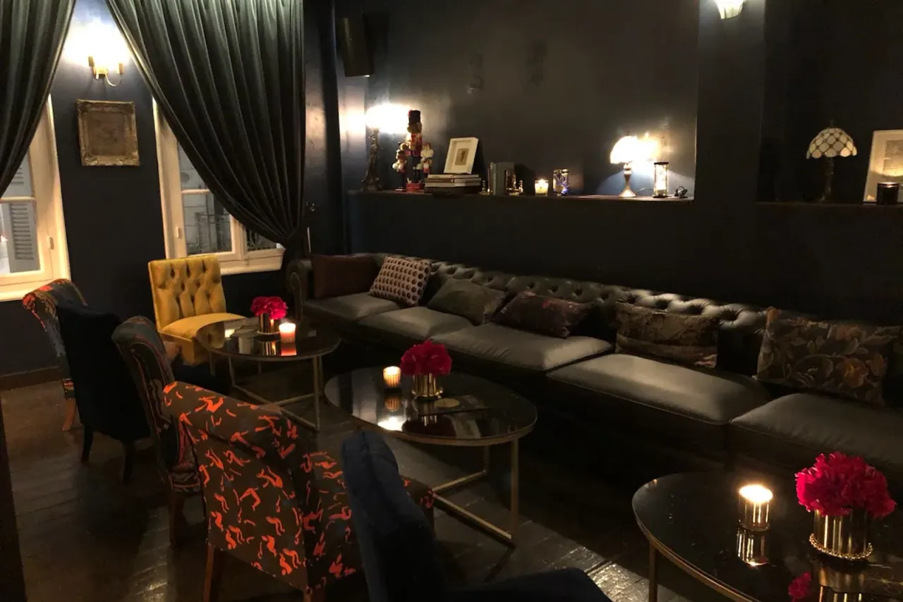 The moody, candlelit lounge of a Thessaloniki cocktail bar with velvet seating and warm lamplight