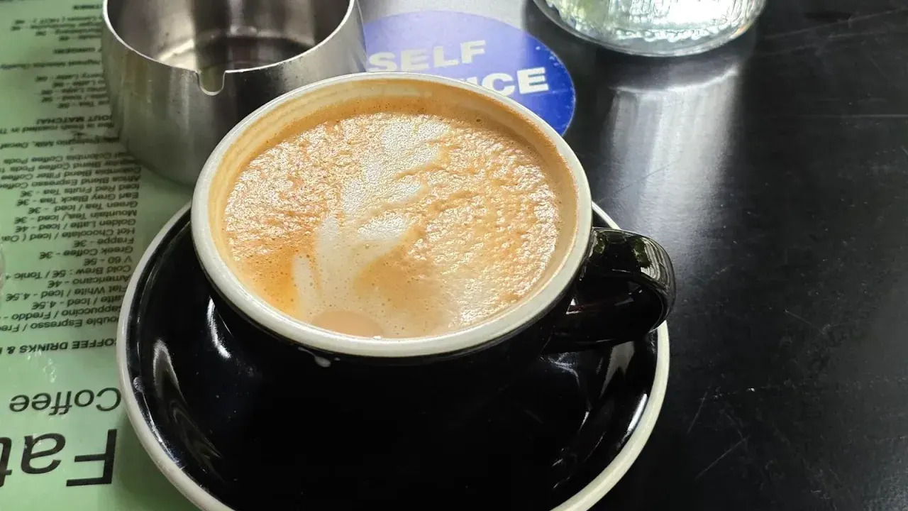 A flat white with latte art in a black cup on a Thessaloniki specialty café table