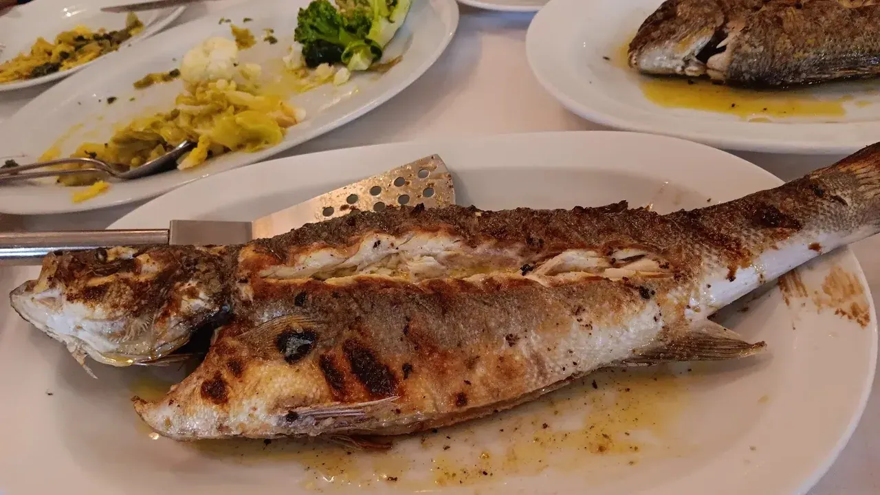 A whole charcoal-grilled fish with steamed broccoli and cauliflower on a plate at a Thessaloniki fish taverna