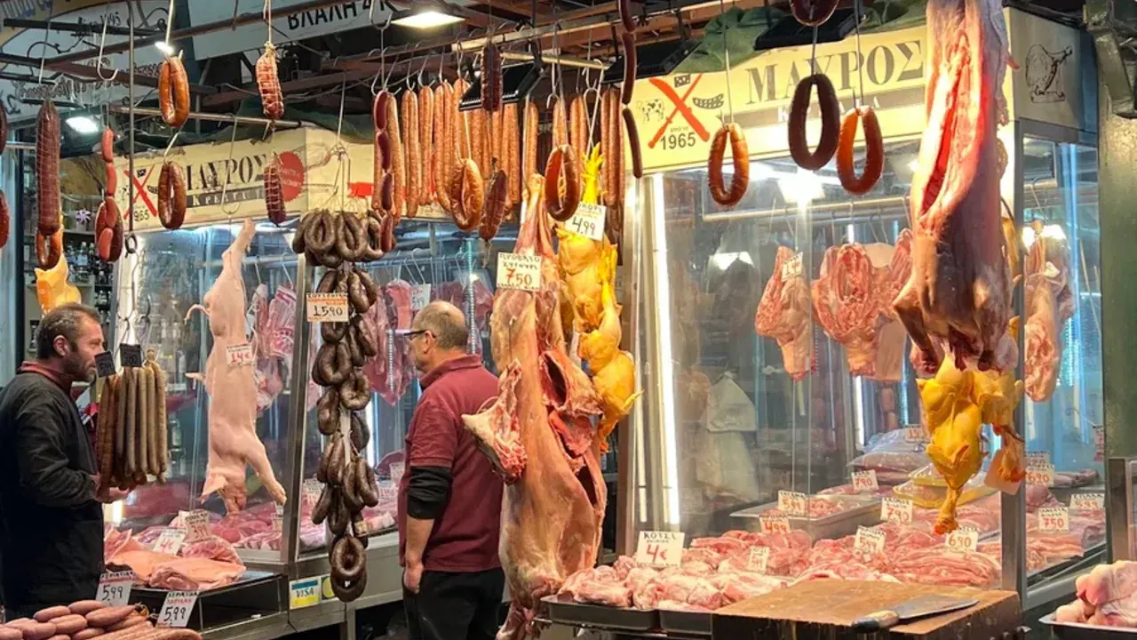 A butcher's stall hung with sausages and meat as a customer talks with the vendor in the covered Kapani market, Thessaloniki