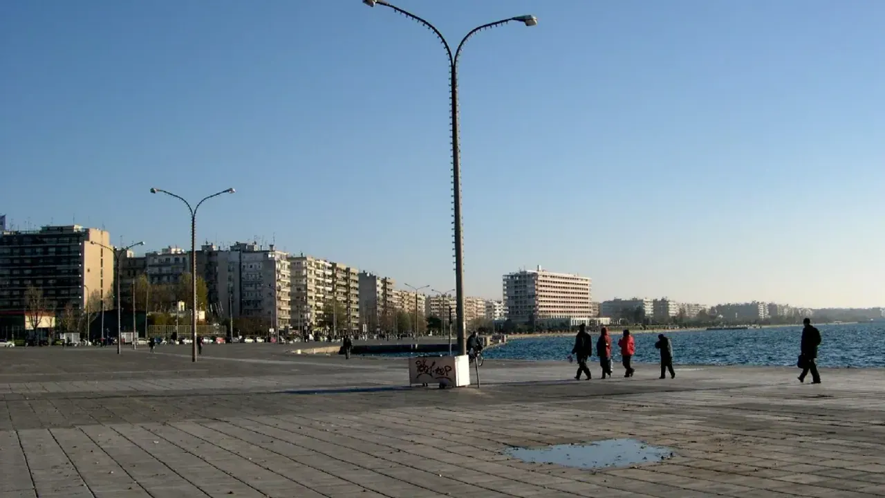 The Thessaloniki waterfront promenade along the Thermaic Gulf, with people walking and the city skyline behind