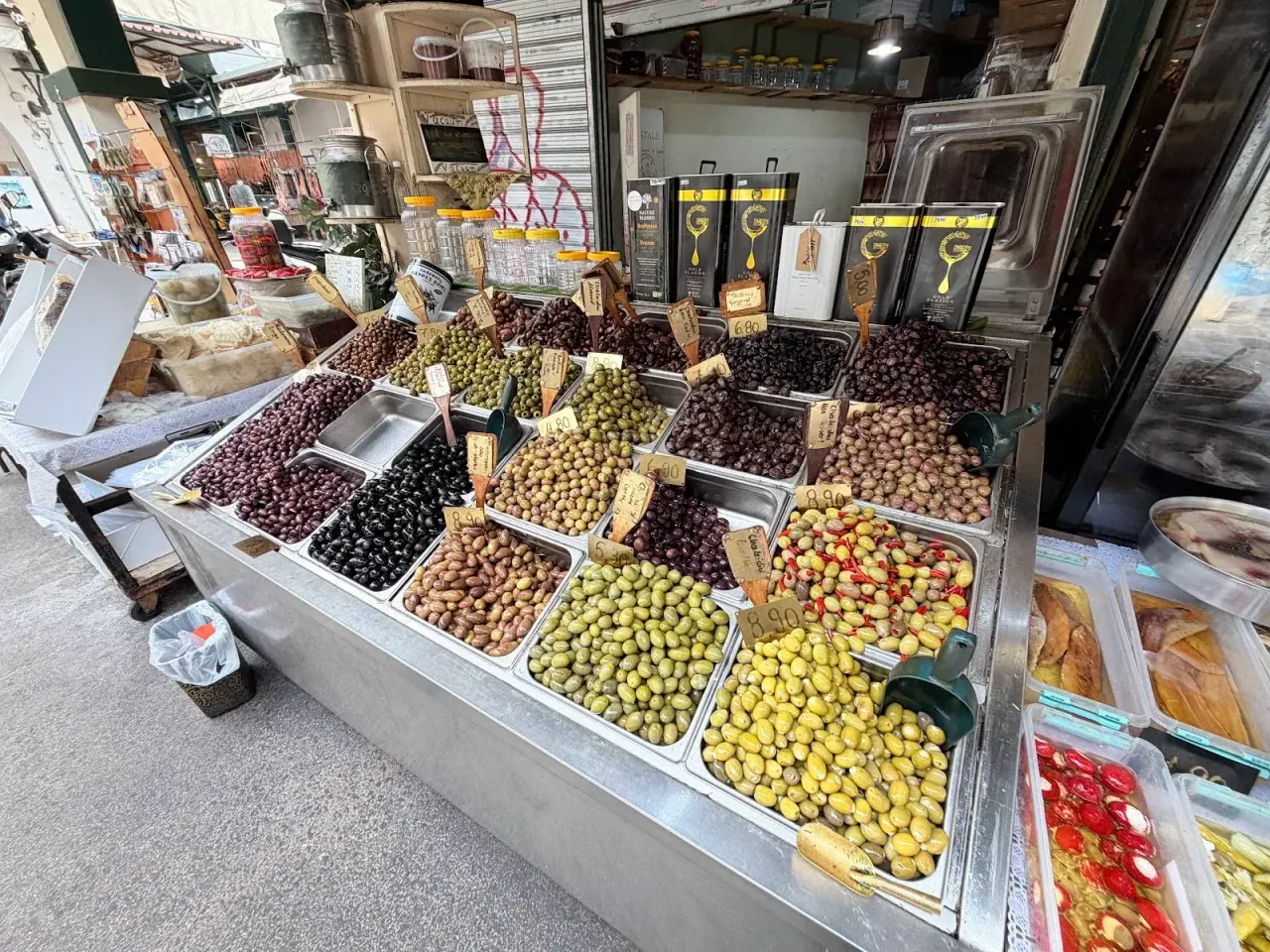 A Kapani market stall in Thessaloniki heaped with trays of olives and hand-written price tags