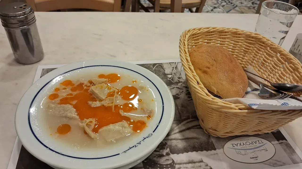 A bowl of patsas tripe soup with bread and water on a marble table at Tsarouchas restaurant in Thessaloniki