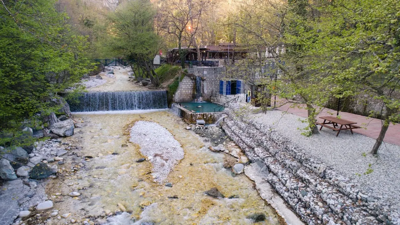 The thermal river gorge at Loutra Pozar, a waterfall spilling past a stone pool and riverside taverna
