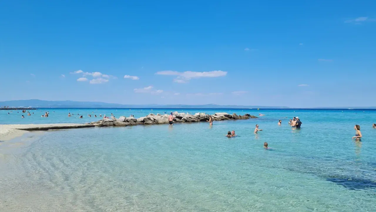 A turquoise beach with clear shallow water and swimmers near Thessaloniki on a bright summer day