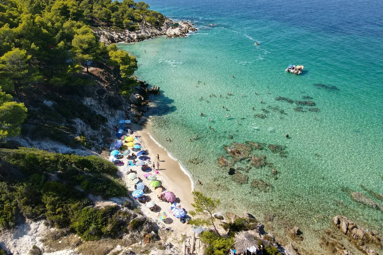 Aerial view of a busy sandy cove with sun umbrellas and swimmers in Halkidiki