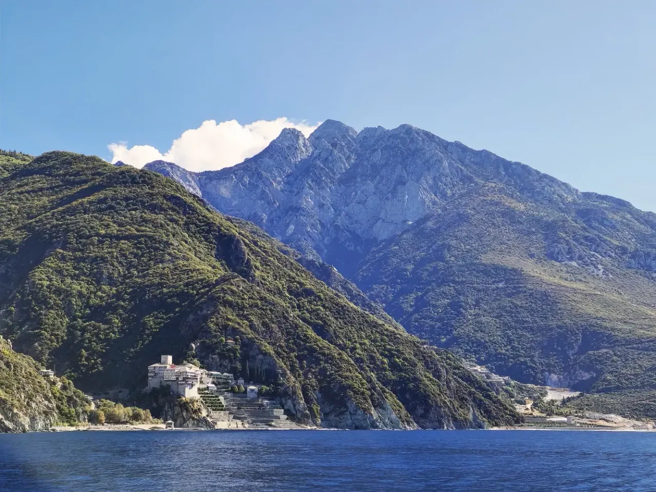 The peak of Mount Athos rising above the peninsula with a shoreline monastery, seen from the sea