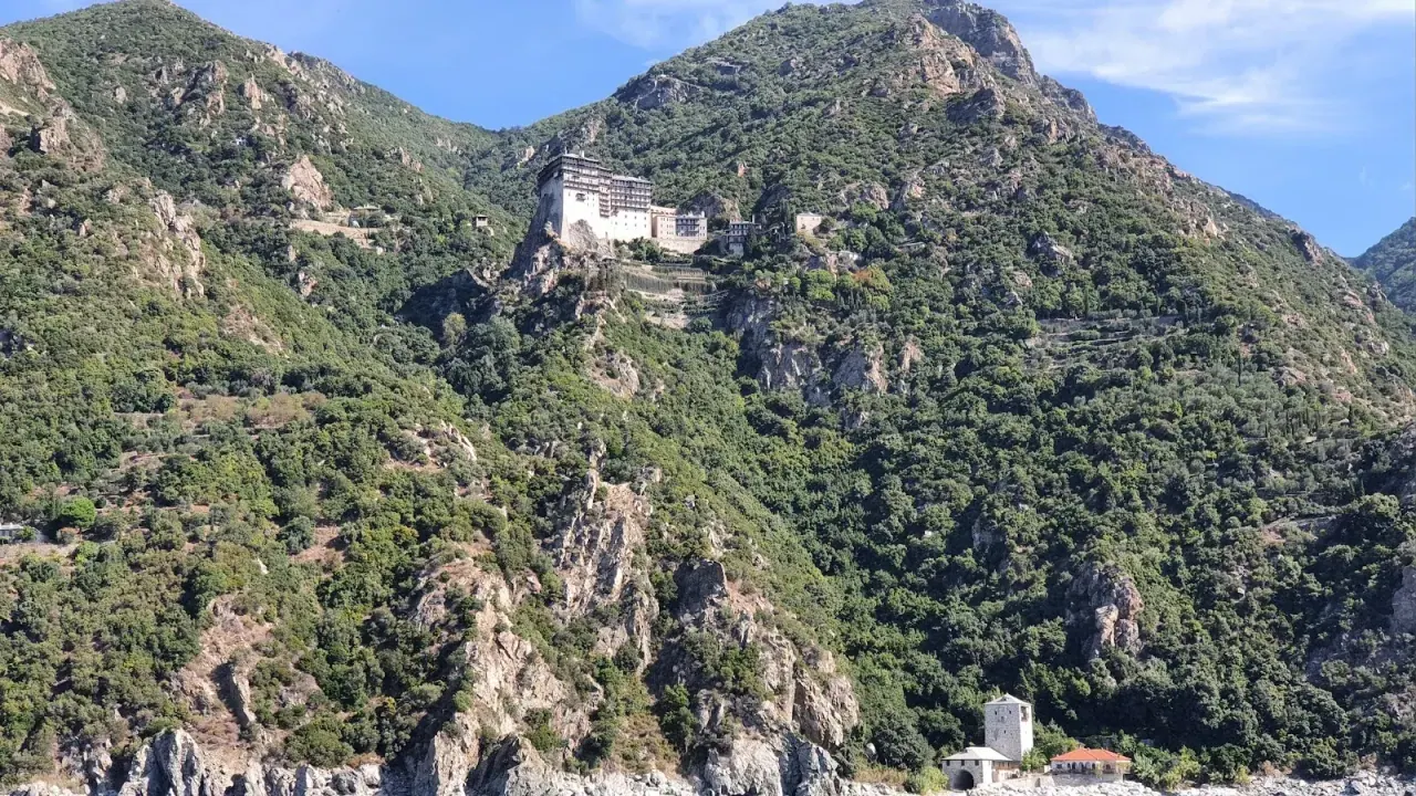 A monastery perched on the green mountainside of Mount Athos, viewed from a passing boat