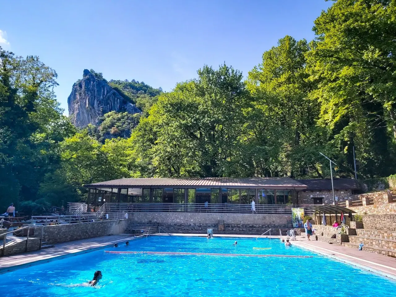 The large outdoor thermal swimming pool at Pozar below a rocky crag and forested hillside