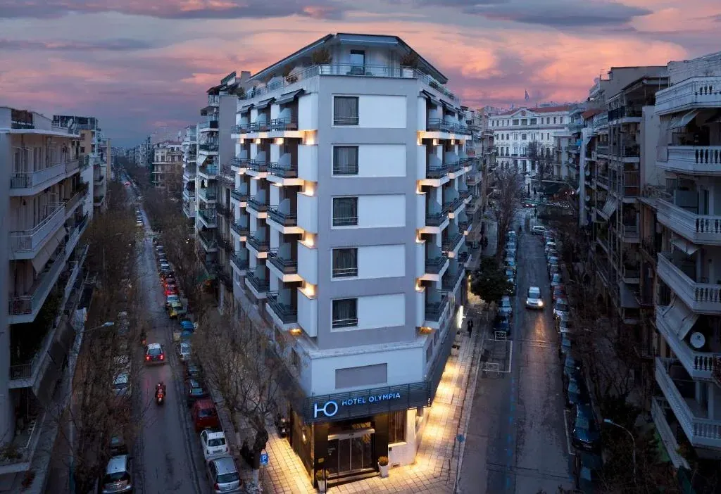 Illuminated corner building of Domotel Olympia at dusk between residential streets in central Thessaloniki