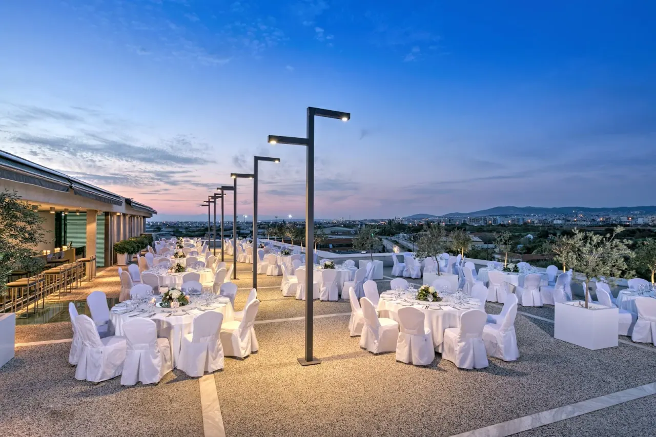 Rooftop event terrace at Porto Palace Hotel set with white-draped tables at dusk overlooking Thessaloniki