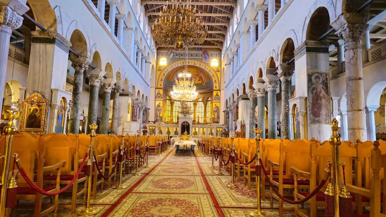 The vast colonnaded nave of Agios Dimitrios, lined with marble columns and lit by hanging chandeliers toward the mosaic-decorated apse, Thessaloniki