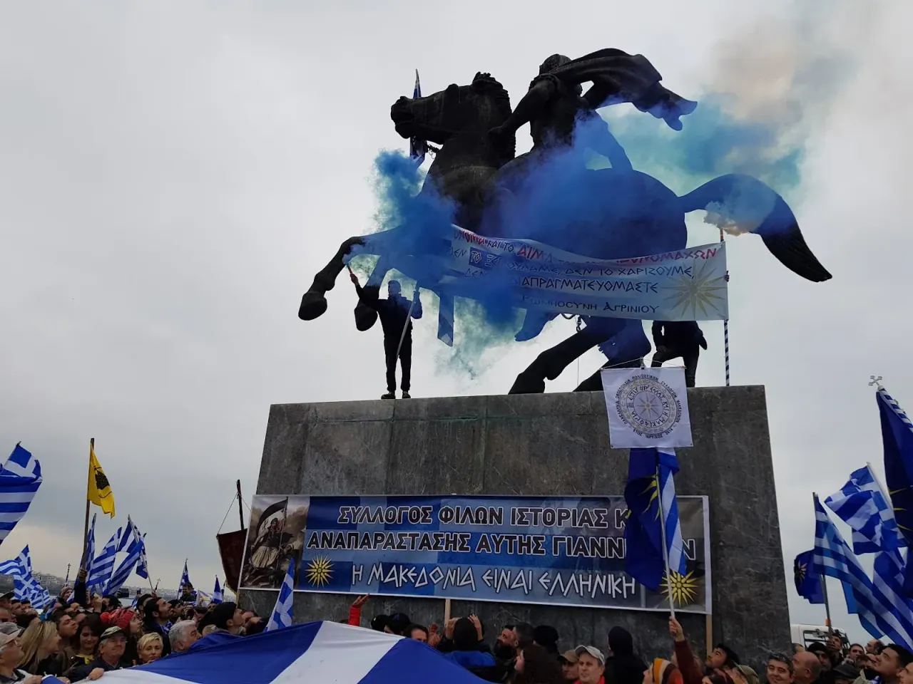 The rearing equestrian statue of Alexander the Great with Greek flags at its base against a blue sky