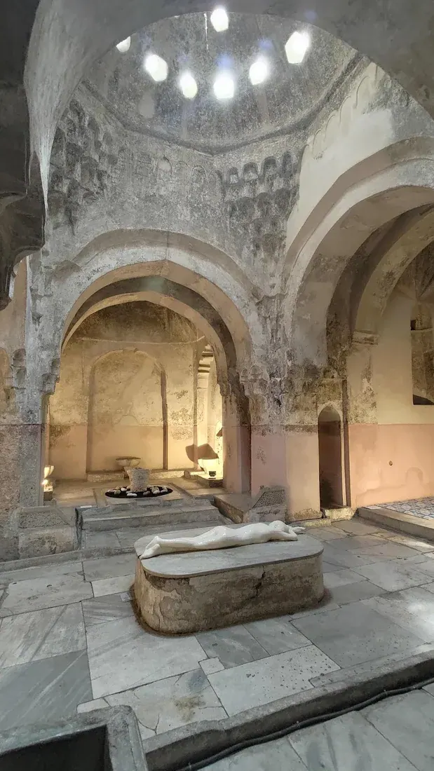 The vaulted marble interior of the Bey Hamam — the hot room with its central navel stone and star-shaped skylights piercing the dome, Thessaloniki