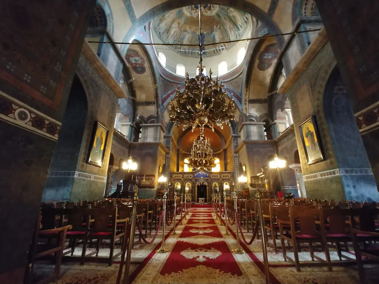 The domed nave of Hagia Sophia in Thessaloniki, looking down the red carpet past the great chandelier to the apse beneath the mosaic dome