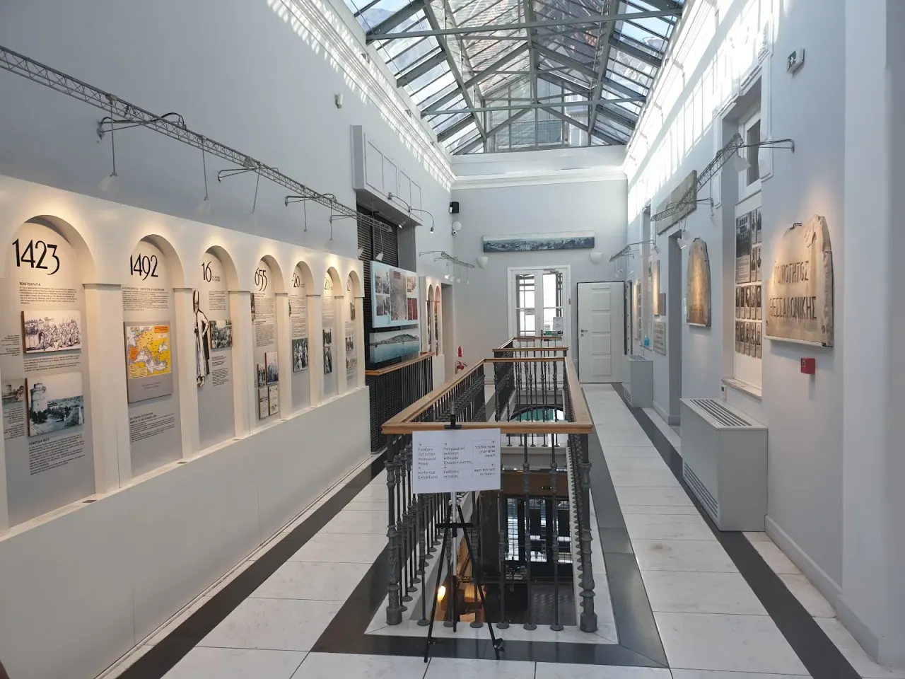 The upper exhibition floor of the Jewish Museum of Thessaloniki, with the community's history timeline displayed under the glass roof