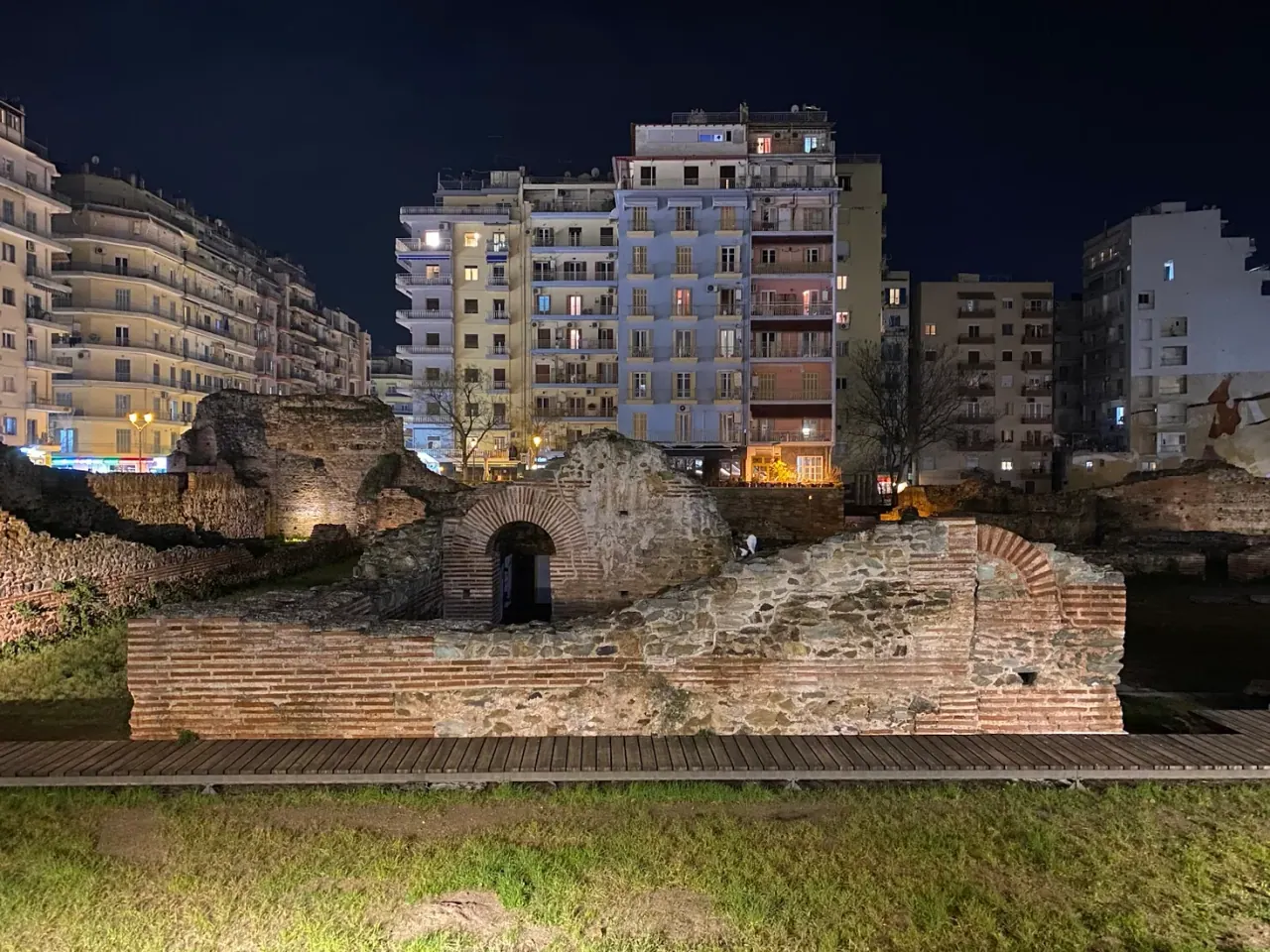 Floodlit brick-and-stone ruins of the Palace of Galerius at Navarinou Square at night, ringed by the modern city
