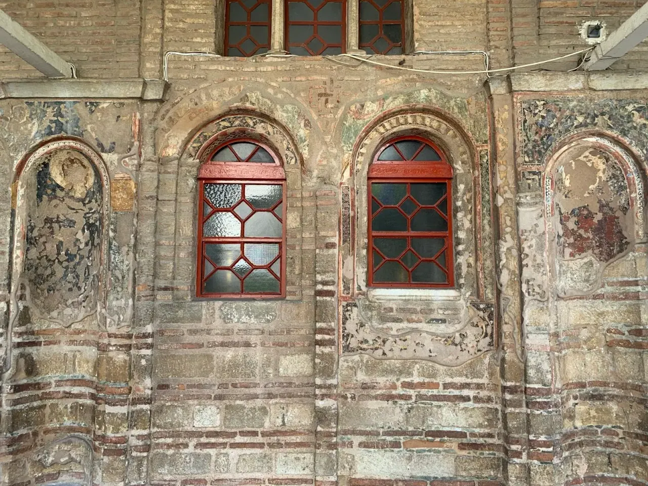 Surviving Byzantine fresco fragments around the arched windows on the brick wall of Profitis Ilias, Thessaloniki