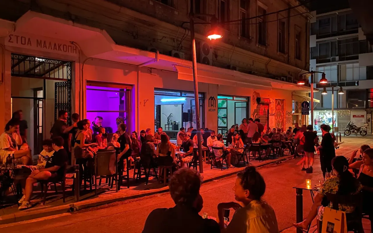 Crowds at outdoor bar tables along the Stoa Malakopi arcade in Valaoritou at night