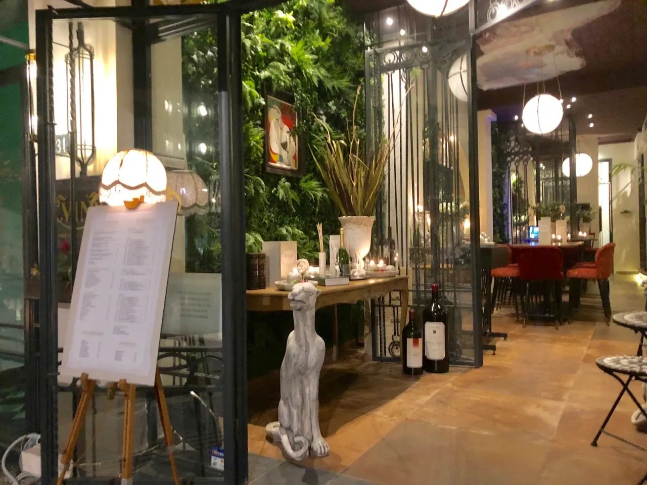 The greenery-framed glass entrance of Vin wine bar on Katouni in Ladadika, Thessaloniki, with a wine menu on an easel and racks of bottles inside