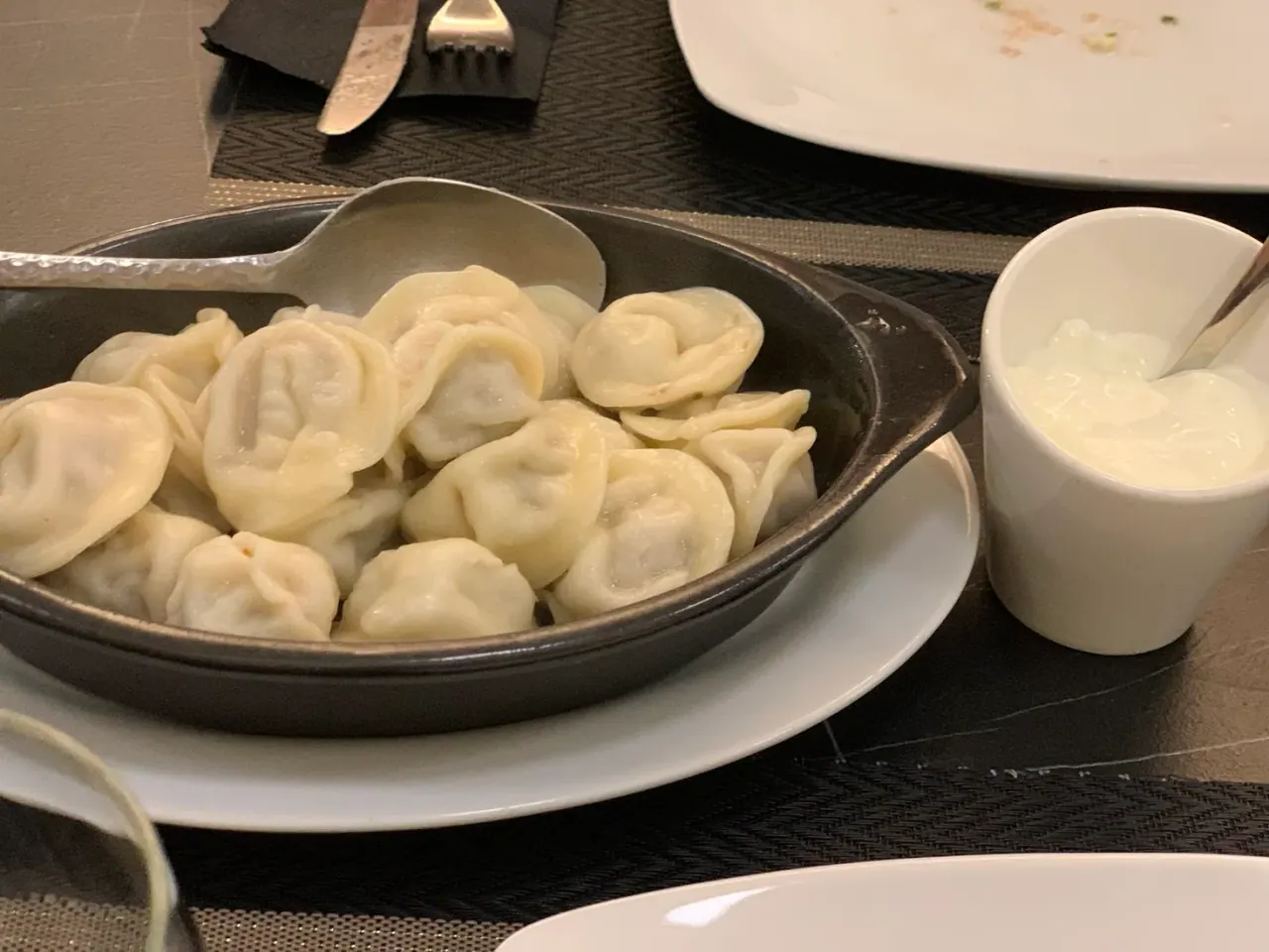 A cast-iron dish of Georgian khinkali dumplings with a pot of sour cream alongside at Assorti, Thessaloniki