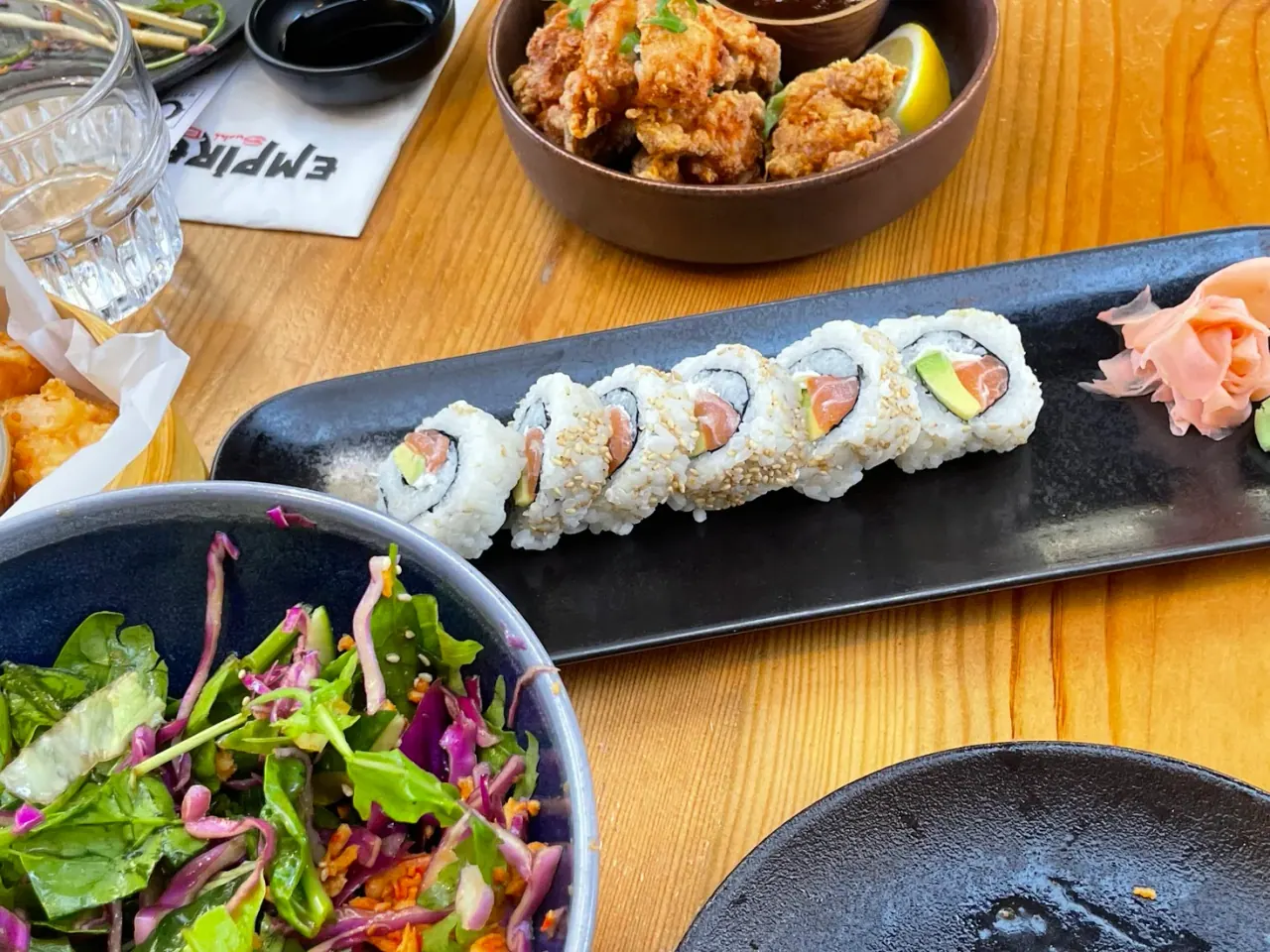 A long plate of sesame-crusted salmon-avocado maki with a bowl of karaage on an Empire Sushi Bar napkin, Thessaloniki