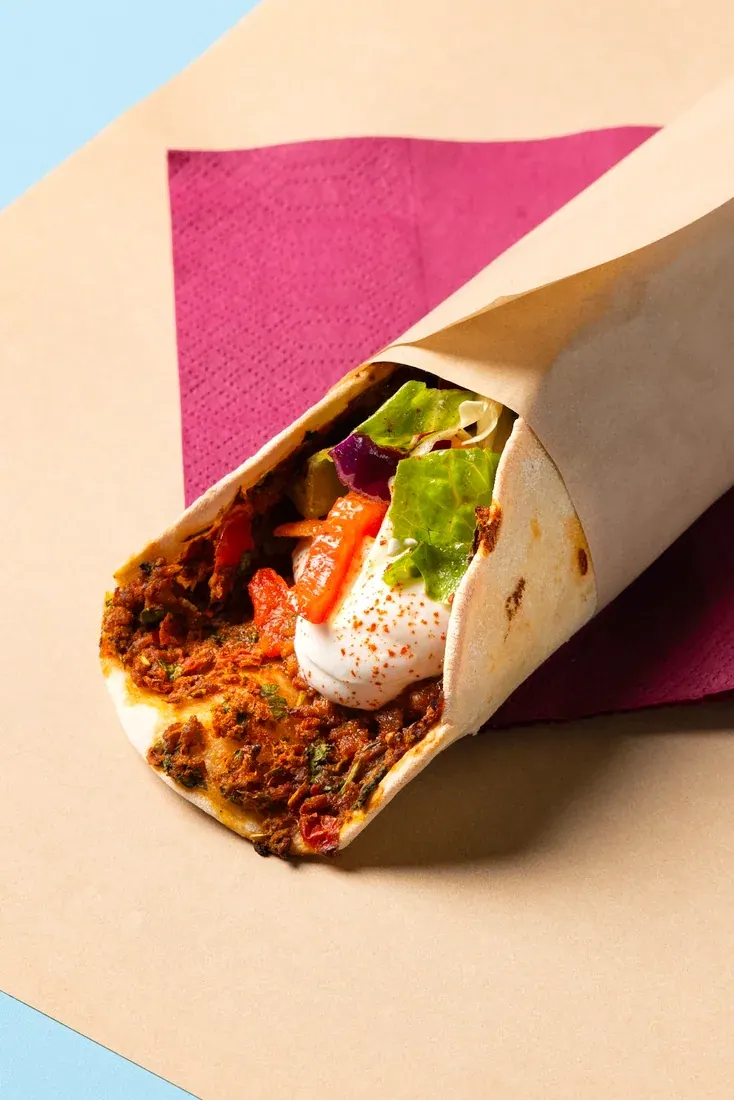 A Levantine spiced-meat wrap in paper on a pink napkin at Feyrouz, Thessaloniki