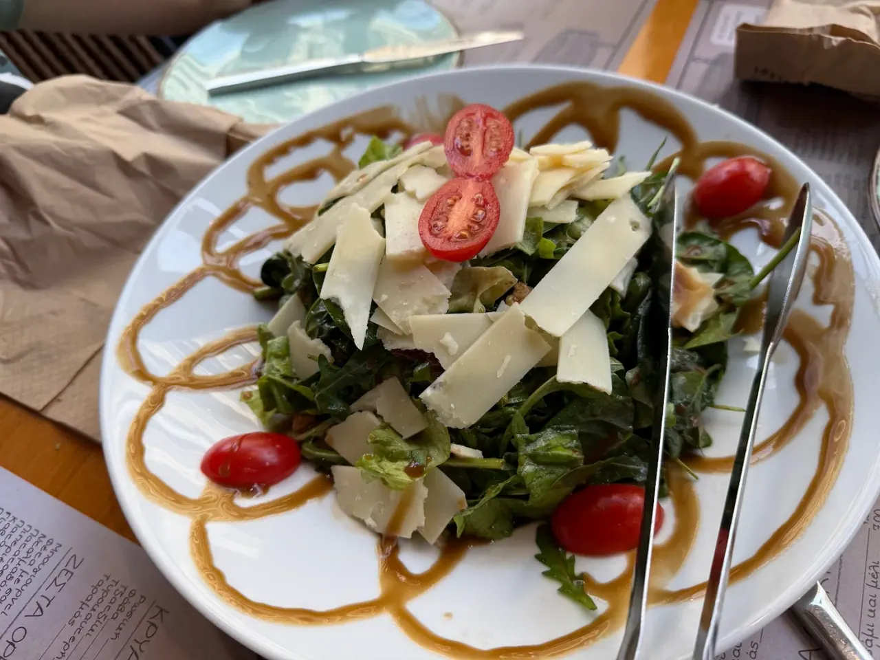 A green salad with shaved cheese and cherry tomatoes over a balsamic-drizzled plate at Kati Ap' Ola, Thessaloniki