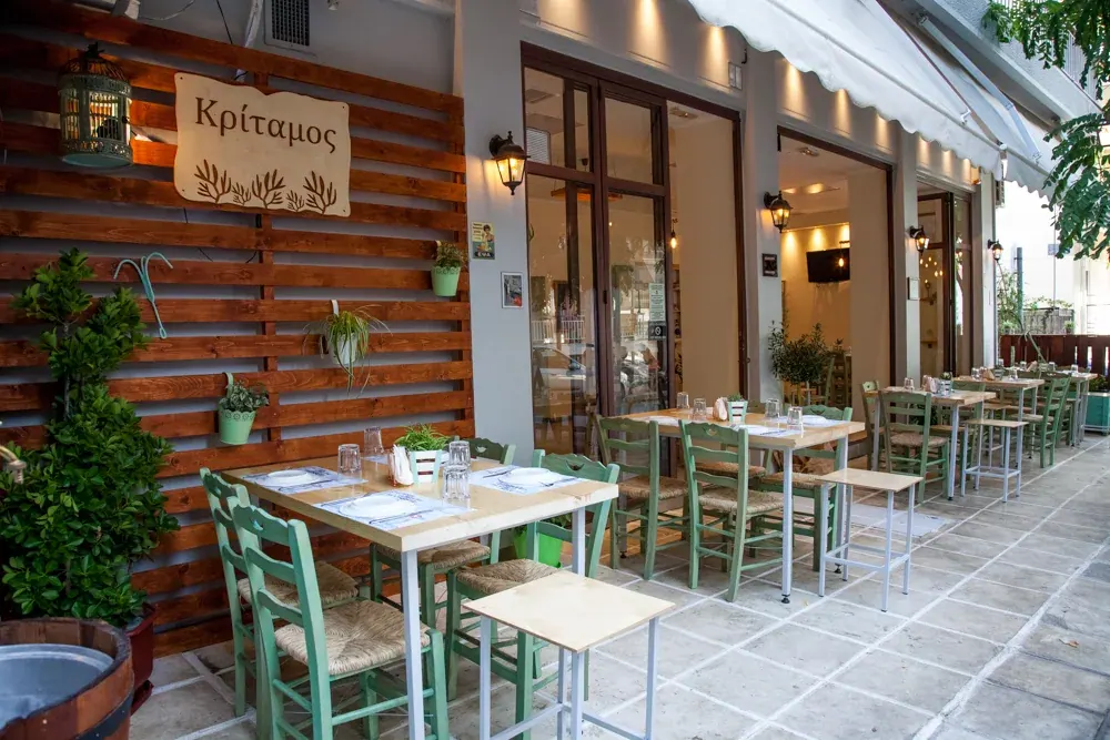 The pavement terrace of Kritamos Meze-Bar in Toumpa — a wooden 'Kritamos' sign, green rush-seat chairs and set tables, Thessaloniki