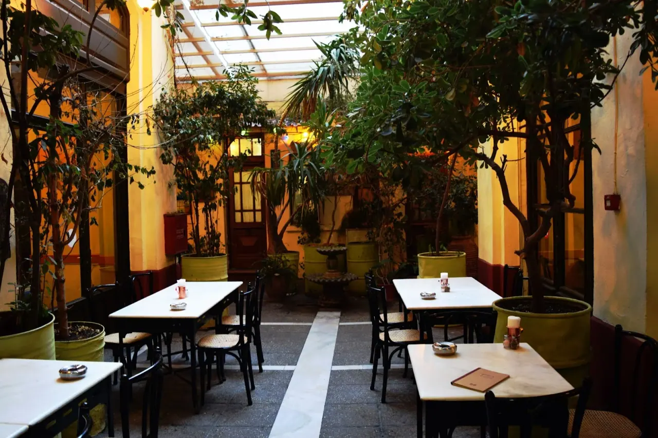 The plant-filled covered courtyard of Ouzeri Aristotelous with marble bistro tables and green planters, central Thessaloniki