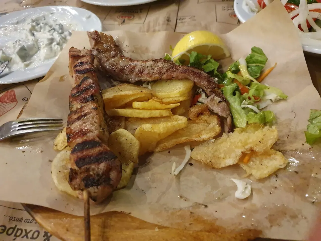 Charcoal-grilled pork skewers with hand-cut chips and salad on kraft paper at Tiganies kai Sxares, Ladadika, Thessaloniki