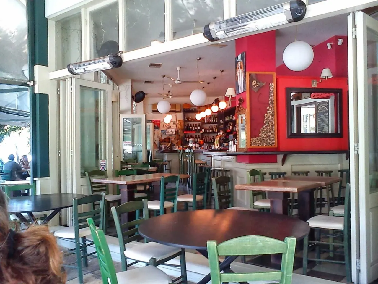 The colourful interior of Toixo Toixo with green rustic chairs and a red accent wall, Ano Poli, Thessaloniki