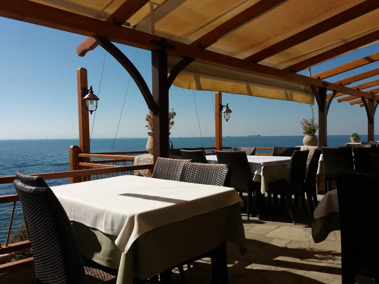 A pergola-shaded seafront terrace with white-clothed tables looking over the Thermaic Gulf at Vrachos, Kalamaria, Thessaloniki
