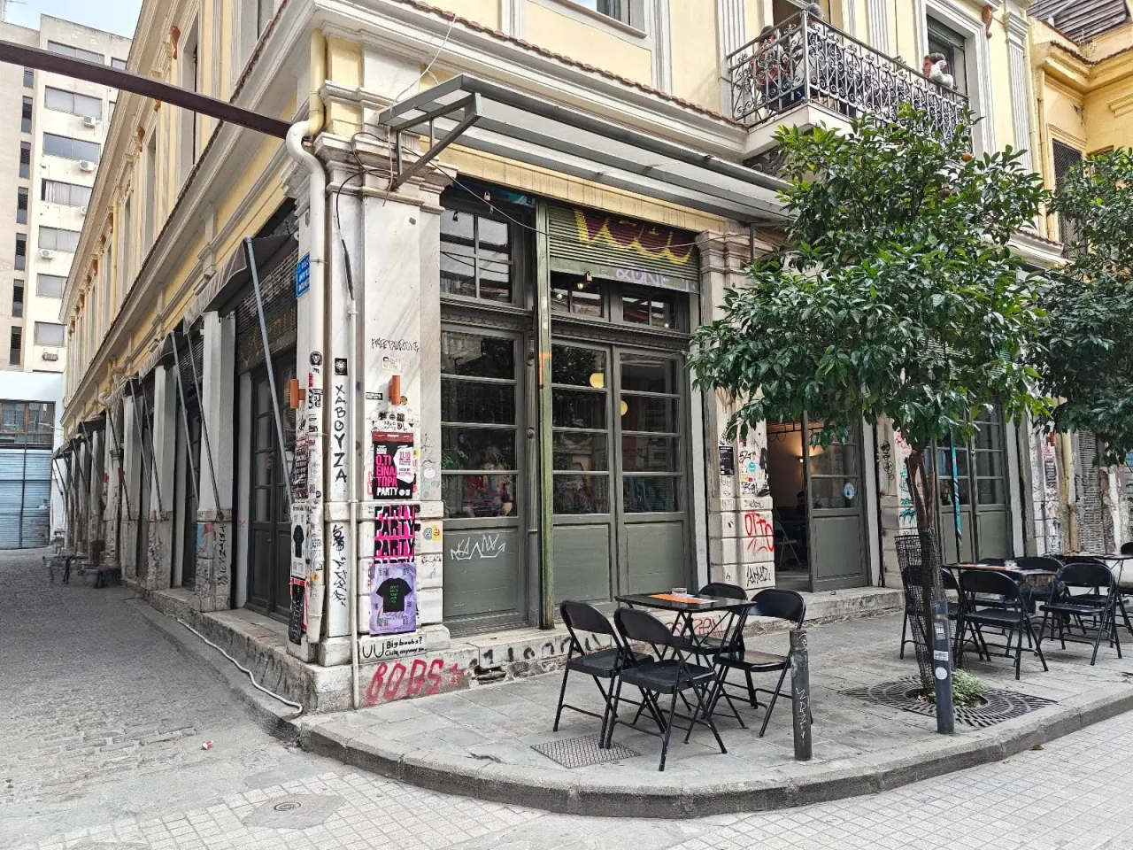 The bohemian corner building of Ypsilon café-bar in central Thessaloniki — columns layered with posters and street art, café tables out front