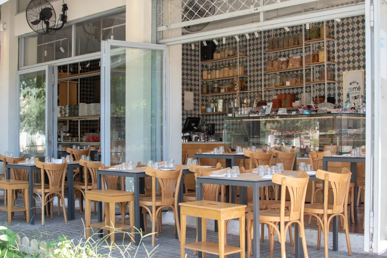 The pavement terrace of Zeme tsipouradiko on Olympou street with wooden chairs and shelves of preserves, Thessaloniki