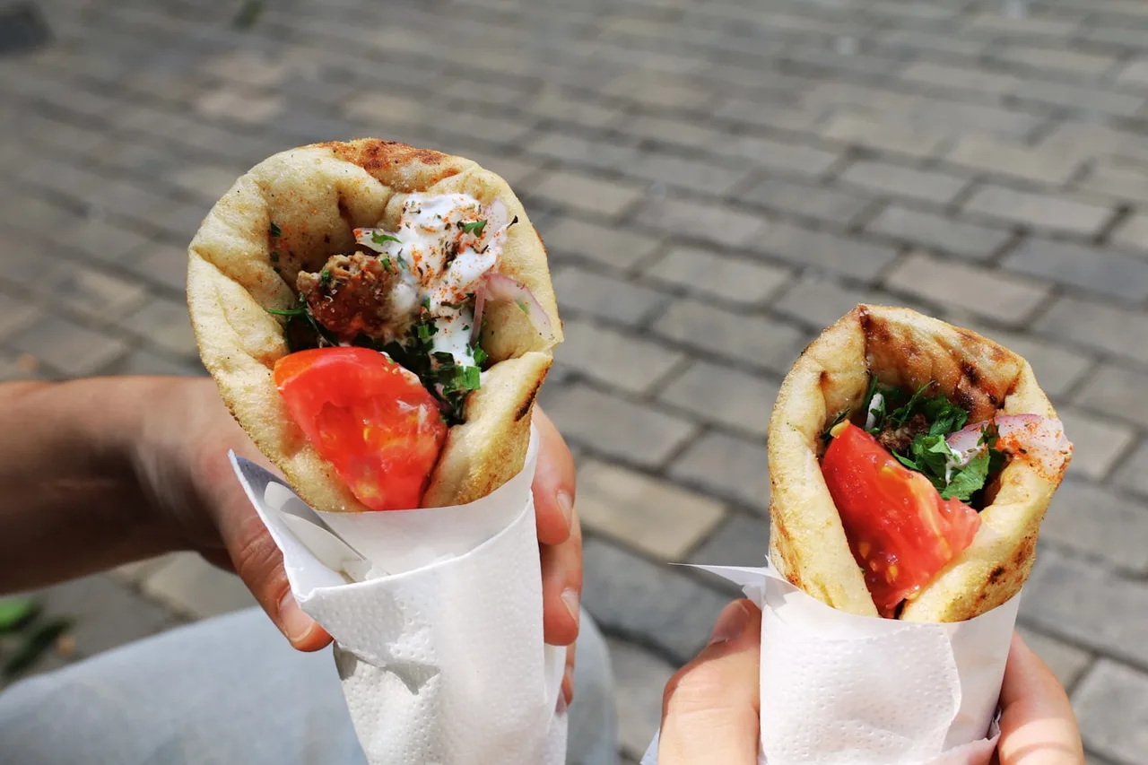 Two freshly wrapped gyros pitas held over a cobbled street