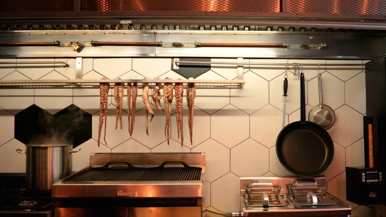 Whole octopus tentacles hanging to dry above a charcoal grill in the open kitchen of Mezen restaurant in Ladadika, Thessaloniki