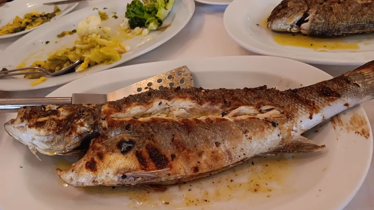 A whole charcoal-grilled fish with steamed broccoli and cauliflower on a plate at a Thessaloniki fish taverna