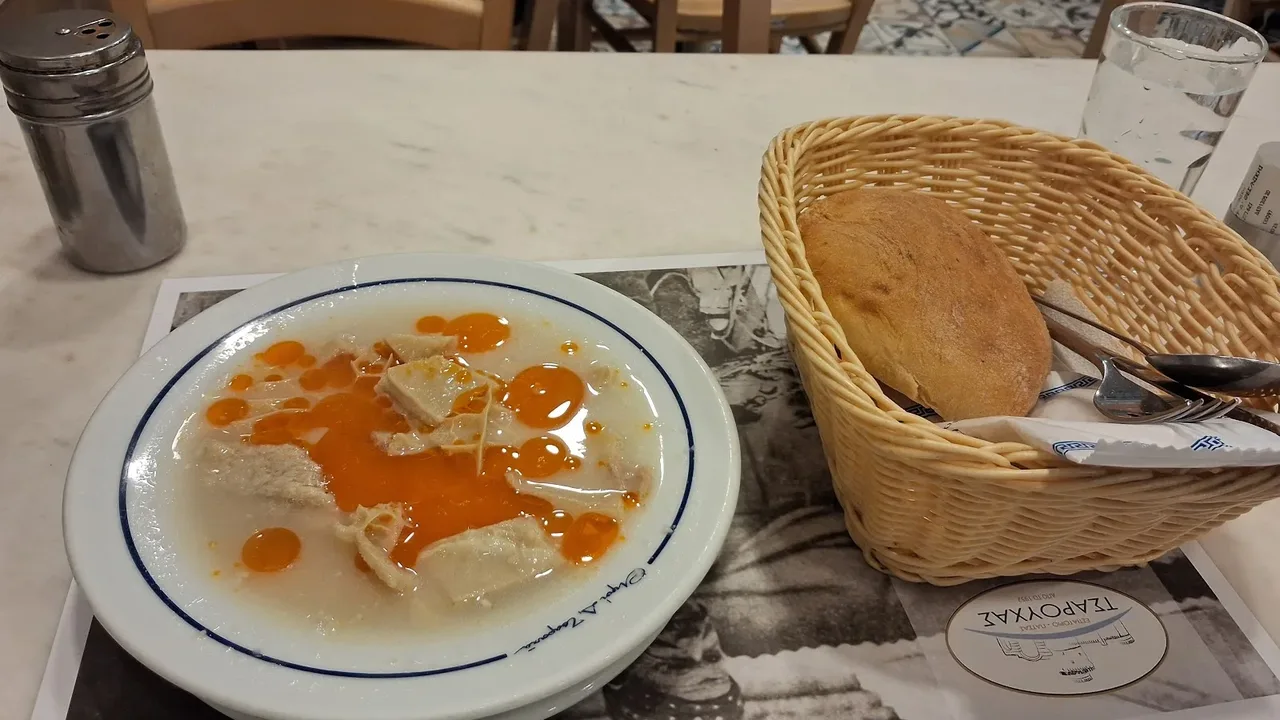 A bowl of patsas tripe soup with bread and water on a marble table at Tsarouchas restaurant in Thessaloniki