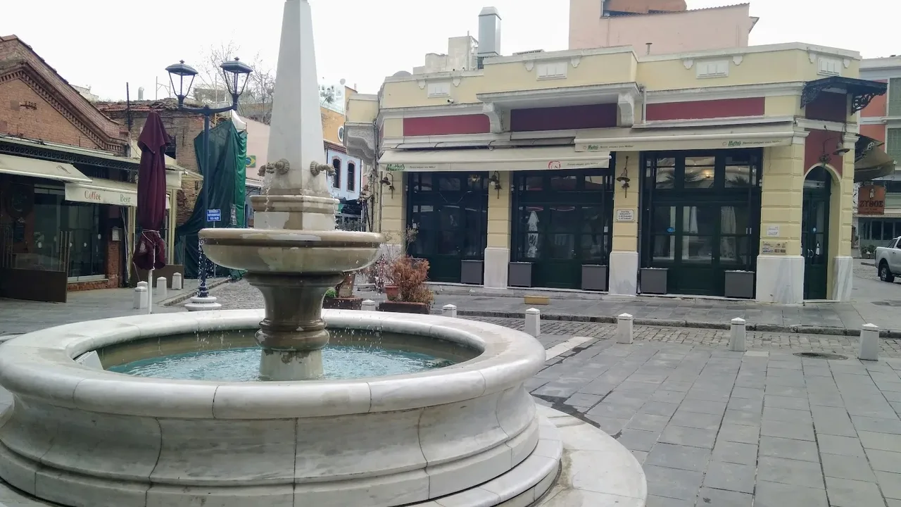 A marble fountain and pastel neoclassical buildings on a square in Thessaloniki's Ladadika district, near the port where several MOMus museums are based