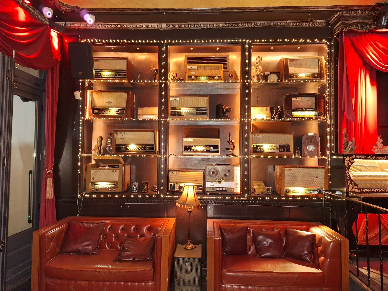 A fairy-lit wall of vintage radios above two leather Chesterfield sofas in the ornate interior of Kafodeio music hall, Thessaloniki